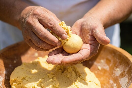 Hands rolling and shaping fresh corn masa dough into a ball in a wooden bowl for tortillas