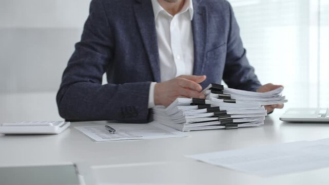 Business professional sorting a large stack of financial reports and tax forms with binder clips on a busy office desk. Audit and taxes