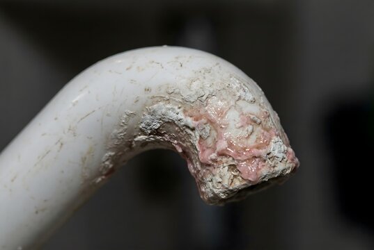 Close-up of a plastic toilet spout encrusted with hard water scale and biofilm