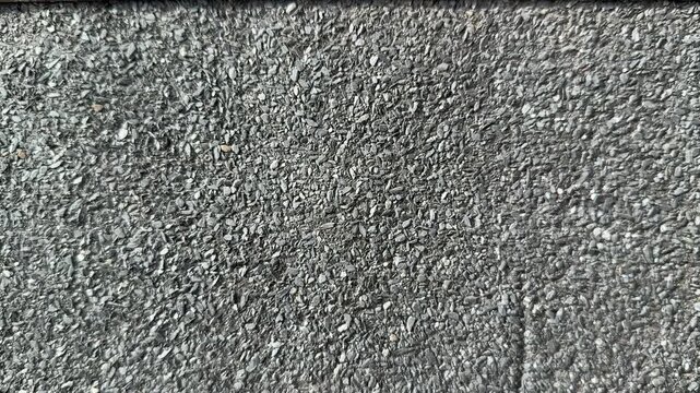 Close-up rolled roofing granules texture, coarse mineral surface on bitumen membrane, grey aggregate fragments, protective coating.