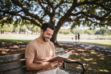 Fototapeta premium A relaxed man enjoys reading a book while sitting on a park bench under a large tree. The peaceful park setting makes this image perfect for themes of relaxation, leisure, and tranquility. Generative