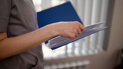 Medical professional in a grey uniform holds a blue folder with patient documents. Close up of a...