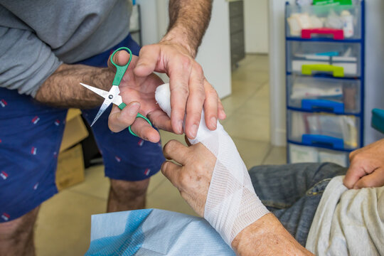 Nurse Cutting Bandage with Scissors While Wrapping Elderly Patient Hand in Outpatient Clinic