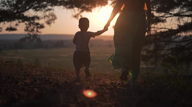 Boy holding mother hand in nature. Family walking together under sunset light. Mother and child go walking across field. Nature peaceful while family walks. Holding hand links mother and child