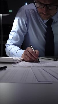 Businessman working overtime in office signing document at night, preparing contracts and finances. Audit and taxes in business