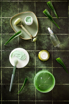 Top view of natural aloe vera skincare products with jade roller and facial mask on green tiled background