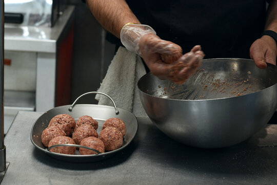 Closeup chef hands shaping meatballs in restaurant kitchen. Food preparation scene highlighting cooking process, ingredients handling, and professional culinary environment.