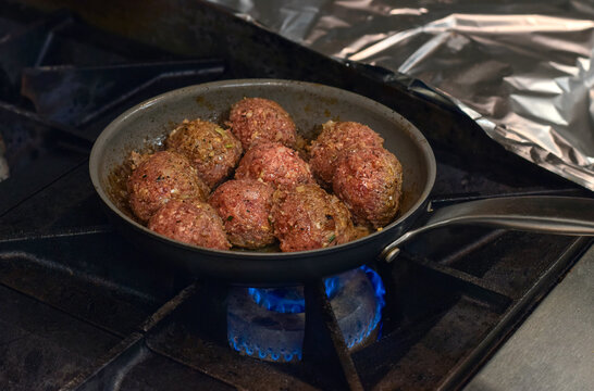 Meatballs cooking in frying pan on gas stove in restaurant kitchen highlighting cooking process, heat, and professional food preparation