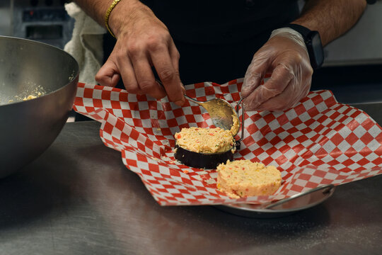 Closeup chef hands preparing crab cakes using round ring mold in restaurant kitchen. Food preparation scene highlighting shaping technique, ingredients handling, and professional culinary environment