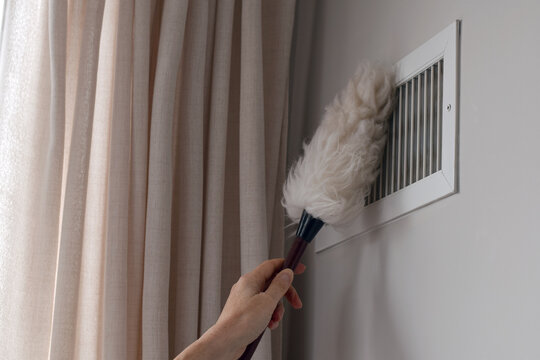 Person hand cleaning ventilation vent using lambswool hand duster. Home maintenance scene removing dust from air vent, highlighting cleaning routine and household upkeep
