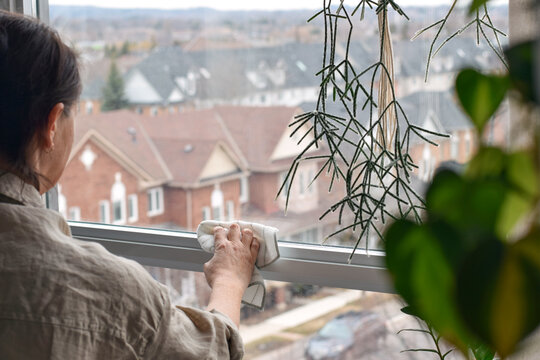 Woman cleaning window frame in apartment using rag. Indoor home cleaning scene focusing on household chores, surface wiping, and maintaining tidy living space.