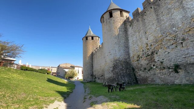 Medieval stone fortress wall with turrets and grassy path under blue sky
