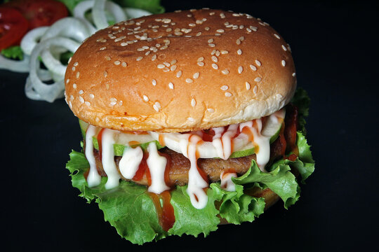 Classic Beef Burger with Sesame Bun Fresh Lettuce and Onion Rings on Black Background.