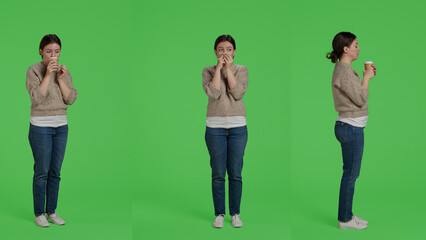 Fototapeta premium Cheerful person drinking cup of coffee over full body green screen backdrop, holding caffeine drink in studio. Young adult enjoying caffeine beverage on isolated greenscreen, portrait.