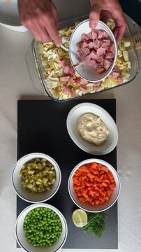 Hands layering ingredients for traditional Olivier Ruska Salad in a Glass Bowl
