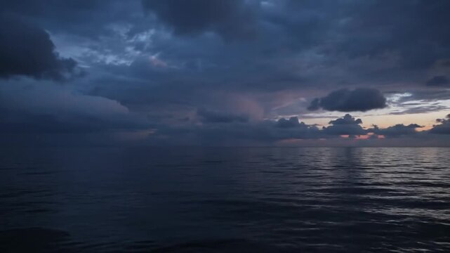 Dark foreboding storm clouds filling the sky above a calm deep blue ocean at twilight, atmospheric seascape with heavy overcast clouds and faint orange light on the horizon.