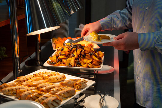 Person serving hot dishes at a hotel buffet with tongs