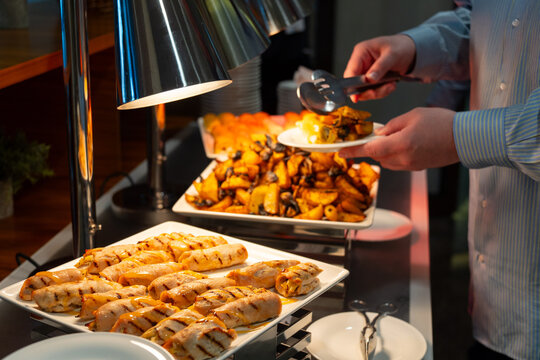 Person serving hot buffet food under warming lamps