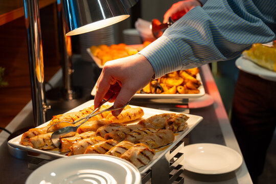 Hand using tongs to serve grilled chicken rolls with sauce at a hot hotel buffet