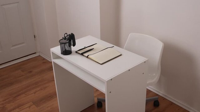 Top view of workspace with open notebook, stapler, scissors in holder and pen, clean minimal office desk setup with copy space.
