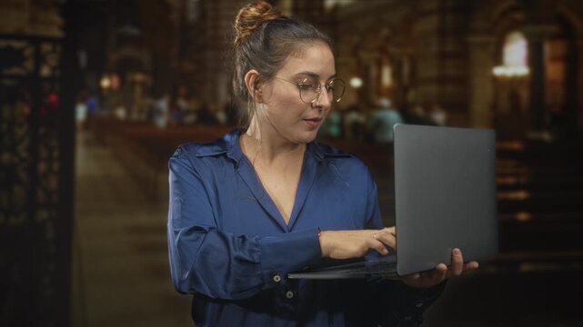 Woman holding laptop and tapping keyboard in a building cathedral interior with pews, arches and stained glass; concentration productivity.