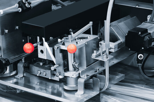 Close-up of industrial automation machinery with metallic components, red knobs, and colorful tubing. Machine parts show precision engineering for manufacturing