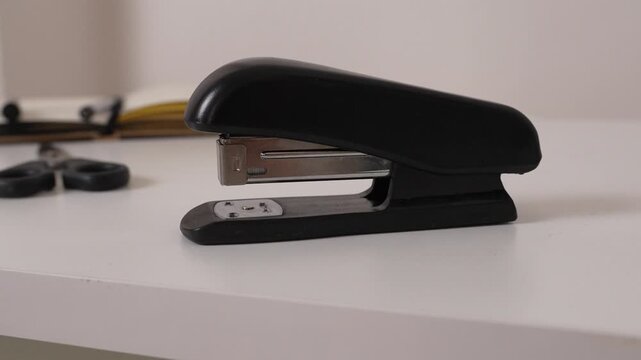 Side profile view of black stapler on desk, minimal office workspace concept, clean composition with business and stationery theme.
