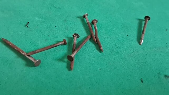 Rusty metal nails scattered across a green surface in this close up high definition motion footage
