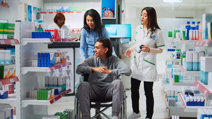 Fototapeta premium Client with disability and social worker receiving medical supplies in pharmacy, buying healthcare products. Customer in wheelchair receiving pharmaceutical drugs, pharmacist giving advice.
