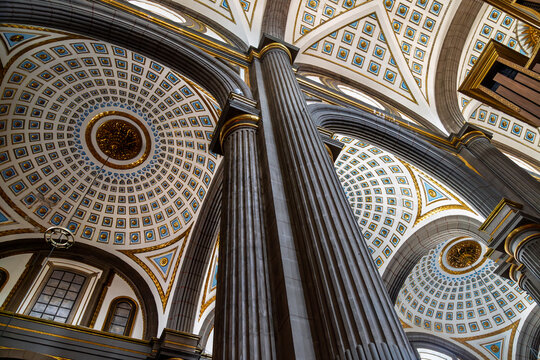 Extreme low angle view of towering fluted columns rising to ornate coffered ceilings with blue and gold geometric patterns inside historic cathedral in Puebla, Mexico