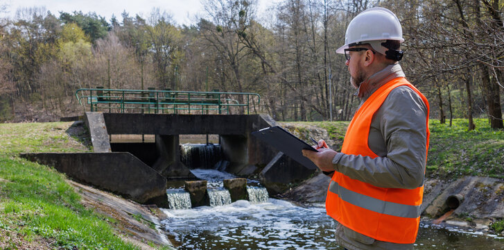 Environmental engineer inspecting a river dam and water level control system for ecological monitoring. Ecologist hydrologist working near a weir for flood prevention and environmental protection.