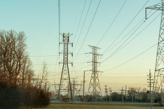 A horizontal shot of multiple transmission towers and power lines silhouetted against a vibrant sunset sky, symbolizing the vital role of sustainable energy in modern infrastructure