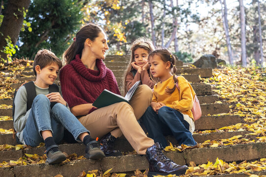 The teacher gently hugs the children, creating a warm and trusting moment outdoors. The scene feels caring and supportive,