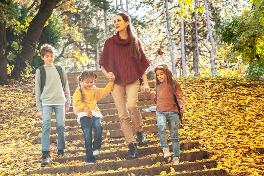 Energetic teacher leads a small, diverse group of preschoolers on an outdoor nature exploration, pointing out interesting details of the local flora and fauna.
