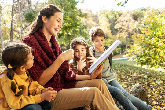 Energetic teacher leads a small, diverse group of preschoolers on an outdoor nature exploration, pointing out interesting details of the local flora and fauna.