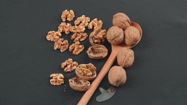 Top-down rotating macro of whole walnuts in shell and shelled kernels on a rustic wooden spoon. Black background. High-quality natural food concept.