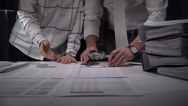 Business people collaborating on a late financial audit, scrutinizing company documents and evidence with a magnifying glass to detect fraud and compliance issues