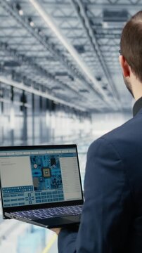 Vertical video Engineer man reviewing semiconductors smart factory schematics with laptop. Manager oversees integrated circuits infrastructure layouts using EDA software on notebook in industry 4.0
