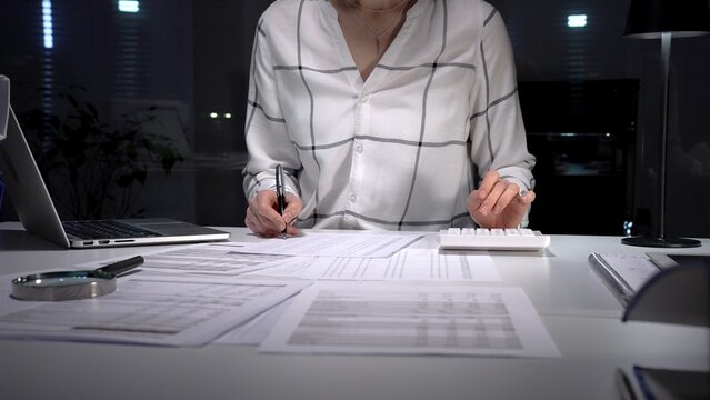 Financial specialist working late crunching numbers and analyzing data, completing important paperwork, calculating taxes, and managing audit preparation in a busy office environment