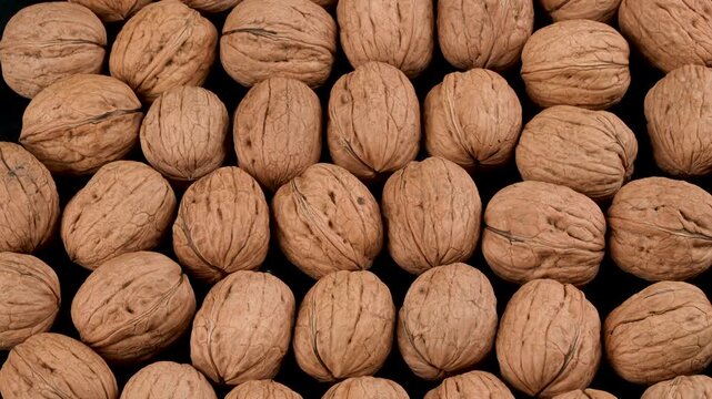 Top-down rotating macro background of whole organic walnuts in their shells. Premium natural food texture concept for diet and nutrition projects.