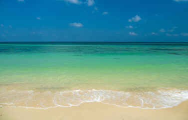Fototapeta premium Idyllic tropical beach with crystal clear turquoise water, soft white sand fluffy clouds bright blue sky, creating peaceful paradise background for summer travel, luxury tourism, and relaxation.