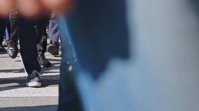 Ground-level view of commuters and office workers walking across a sunlit urban crosswalk. This cinematic slow-motion sequence captures the rhythmic energy of a modern global workforce in motion