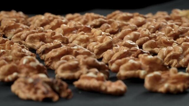 Low angle horizontal view of shelled walnut kernels arranged in rows rotating on black background with selective focus. Premium cinematic organic food texture.