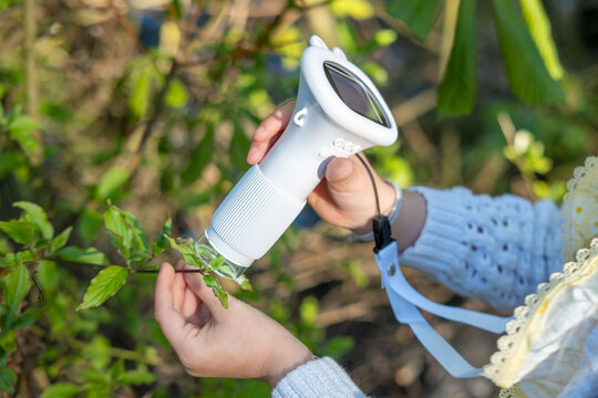 girl Child holding digital microscope, examining texture on LCD screen, educational science toy, young explorer using child-friendly camera to capture beauty nature, blending play outdoor education