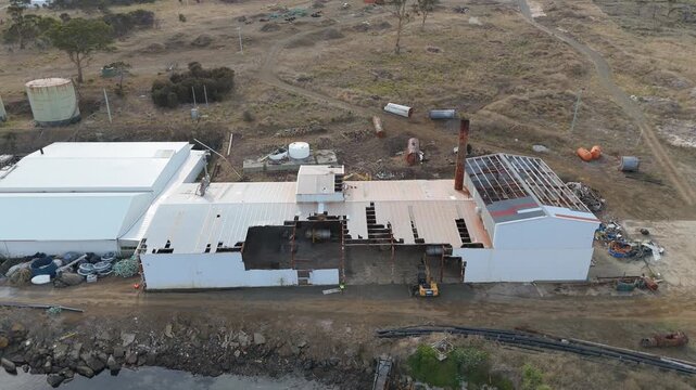 Close-up drone shot of a derelict industrial building with a collapsing roof and chimney.