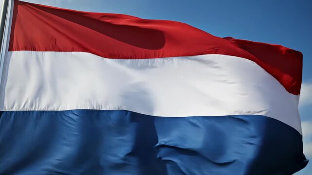 Close-up cinematic footage of a large red-white-blue tricolor flag billowing in the wind against a clear blue sky, detailed fabric folds and dynamic movement in motion
