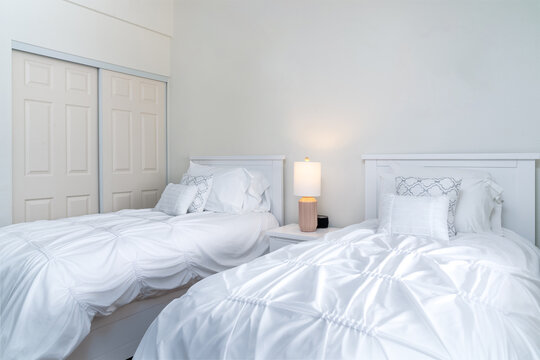Modern white bedroom with twin beds, decorative pillows, bedside lamp