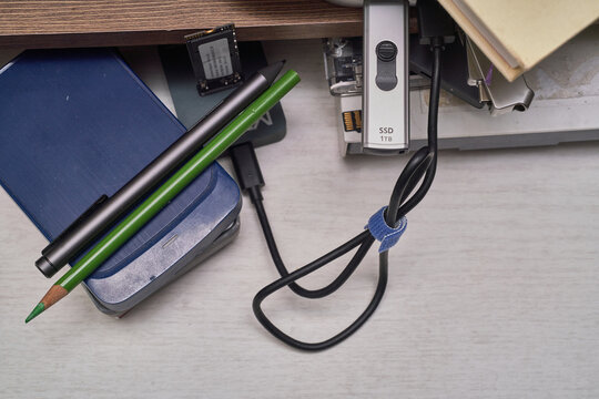 A realistic white desk showcases the evolution of data storage, featuring stacked external hard drives, a modern NVMe SSD, and tied cables. This authentic setup perfectly highlights an IT workspace.
