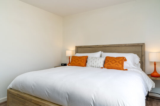 Modern white bedroom with wooden bed frame, decorative pillows, lamps