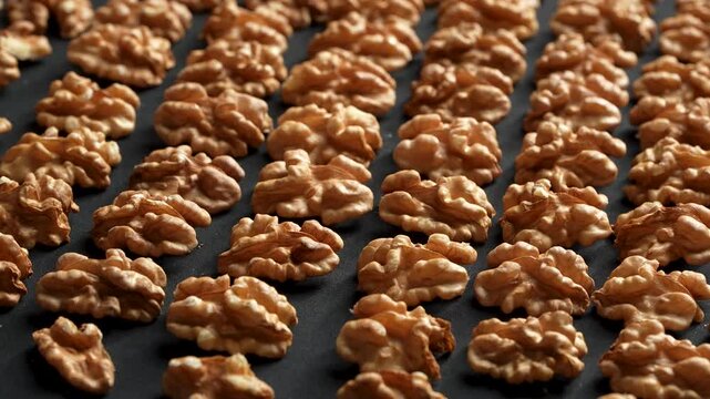 Neatly arranged rows of shelled walnut kernels rotating on a black background. Premium geometric organic food texture.